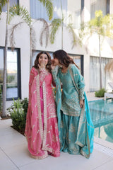 Two women in traditional pink and blue outfits standing outdoors near a pool.