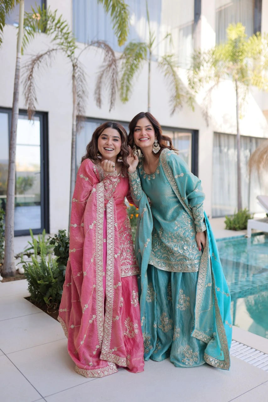 Two women in traditional pink and blue outfits standing outdoors near a pool.