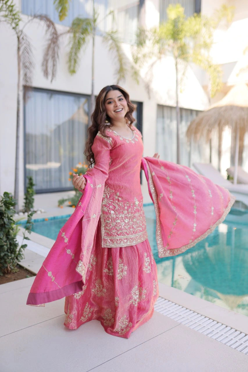 Woman in a pink traditional outfit standing by a pool with a modern building in the background