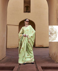 Woman in a light green saree standing in an archway with a beige wall and wooden floor.