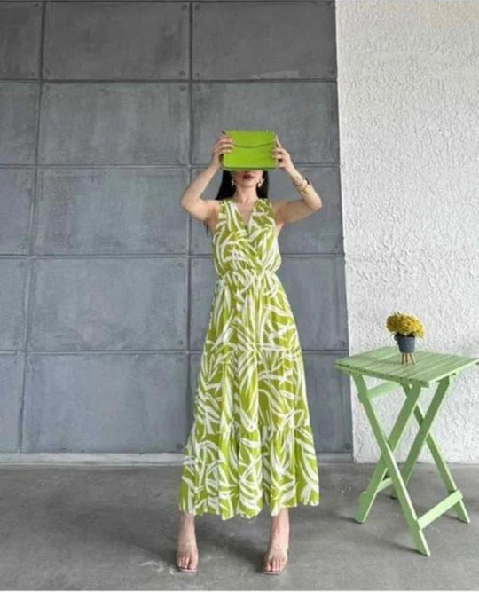 Woman in a green and white dress standing next to a small green table against a gray wall.