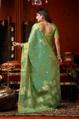 Woman in a green saree with elephant patterns standing in an ornate room.