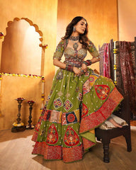Woman in a traditional green and red outfit with intricate patterns in a decorated room.