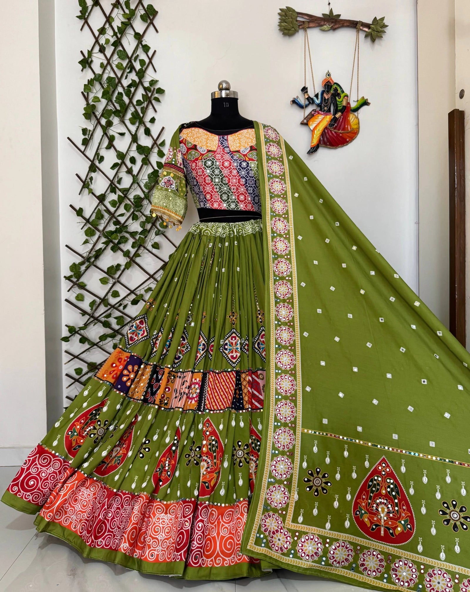 Green embroidered traditional outfit on a mannequin against a white wall with decorative elements.