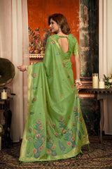 Woman wearing a green saree with floral patterns in an indoor setting.