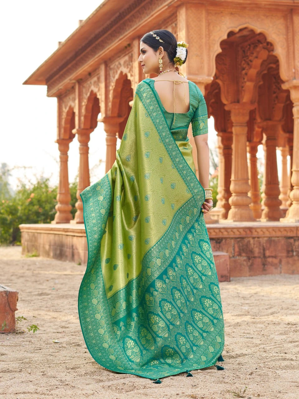 Woman in a green saree standing in front of an architectural structure.