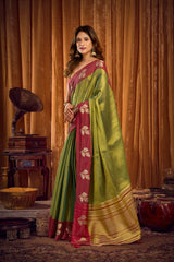 Woman in a green and red saree standing in a vintage room with a gramophone.