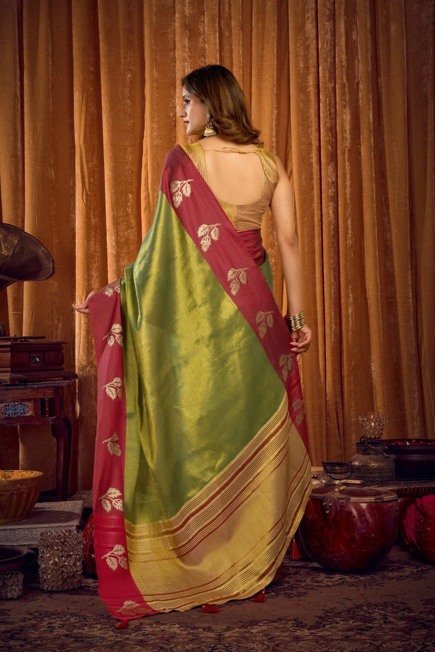 Woman in a green and red saree with a gold blouse against a warm-toned curtain background.