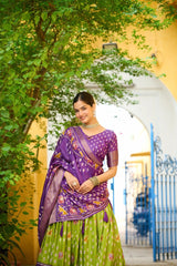 Woman in a purple and green saree standing in front of a decorative archway with greenery.