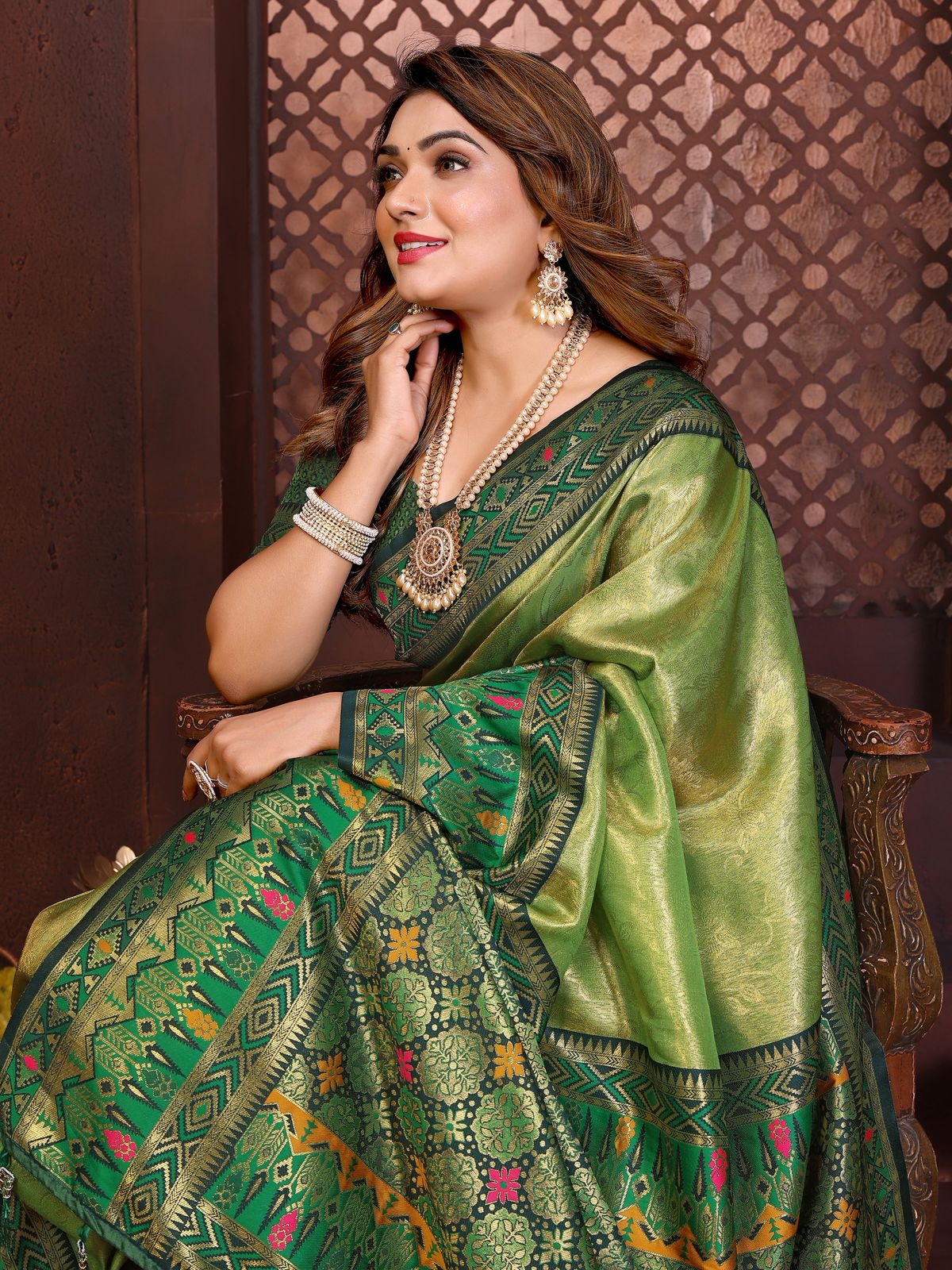Woman wearing a green saree with intricate patterns against a decorative wall.