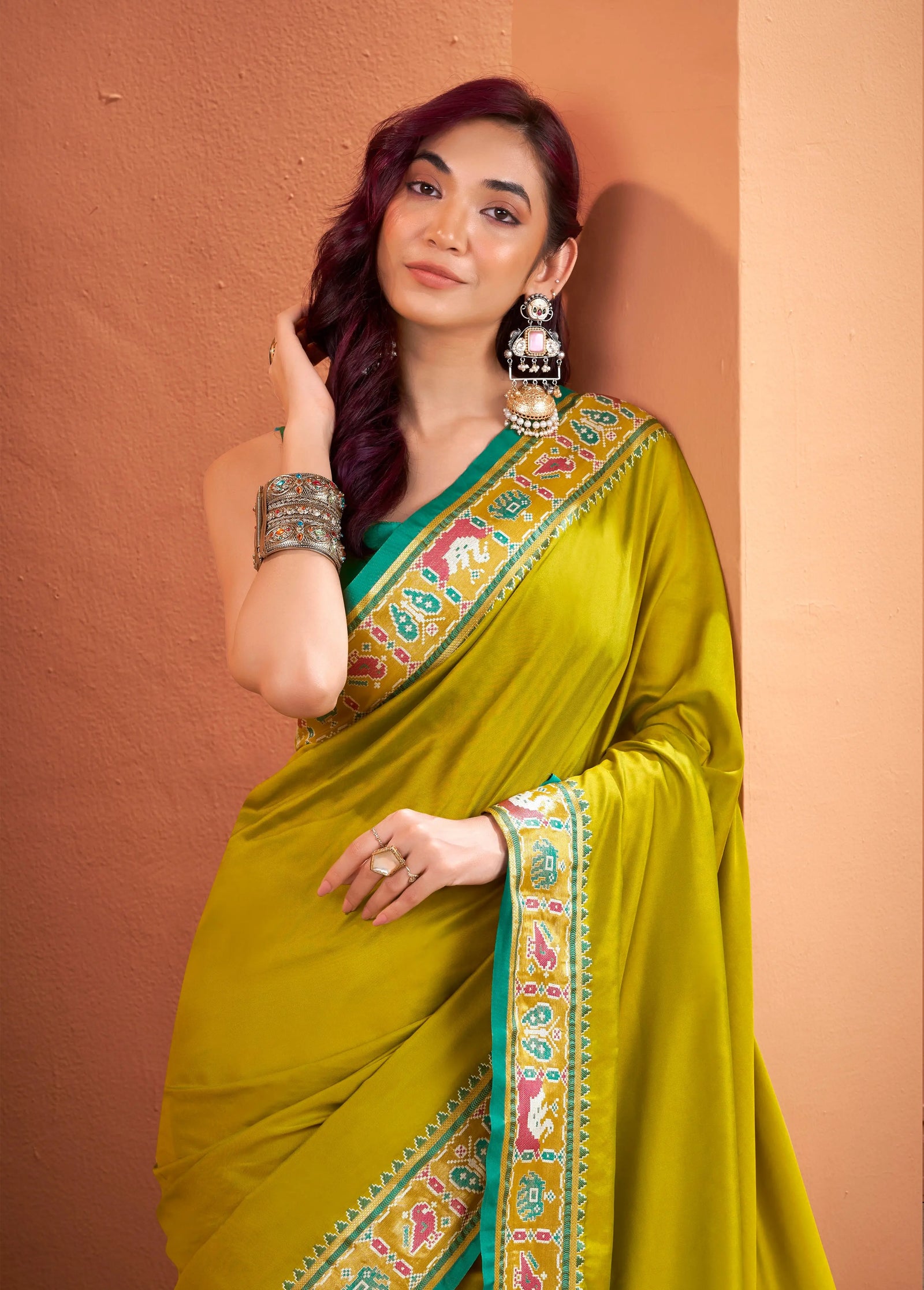 Woman wearing a green saree with a colorful border against a brown background