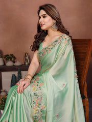 Woman wearing a light green saree with floral embroidery, sitting against a brown background.