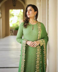 Woman in a green traditional outfit with gold embroidery standing in an outdoor setting.