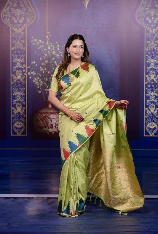 Woman in a light green saree with colorful patterns against a decorative blue wall.