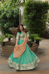 Woman in a green traditional outfit with a peach dupatta standing in a garden setting.