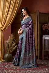 Woman in a purple and blue saree standing in a room with decorative elements.