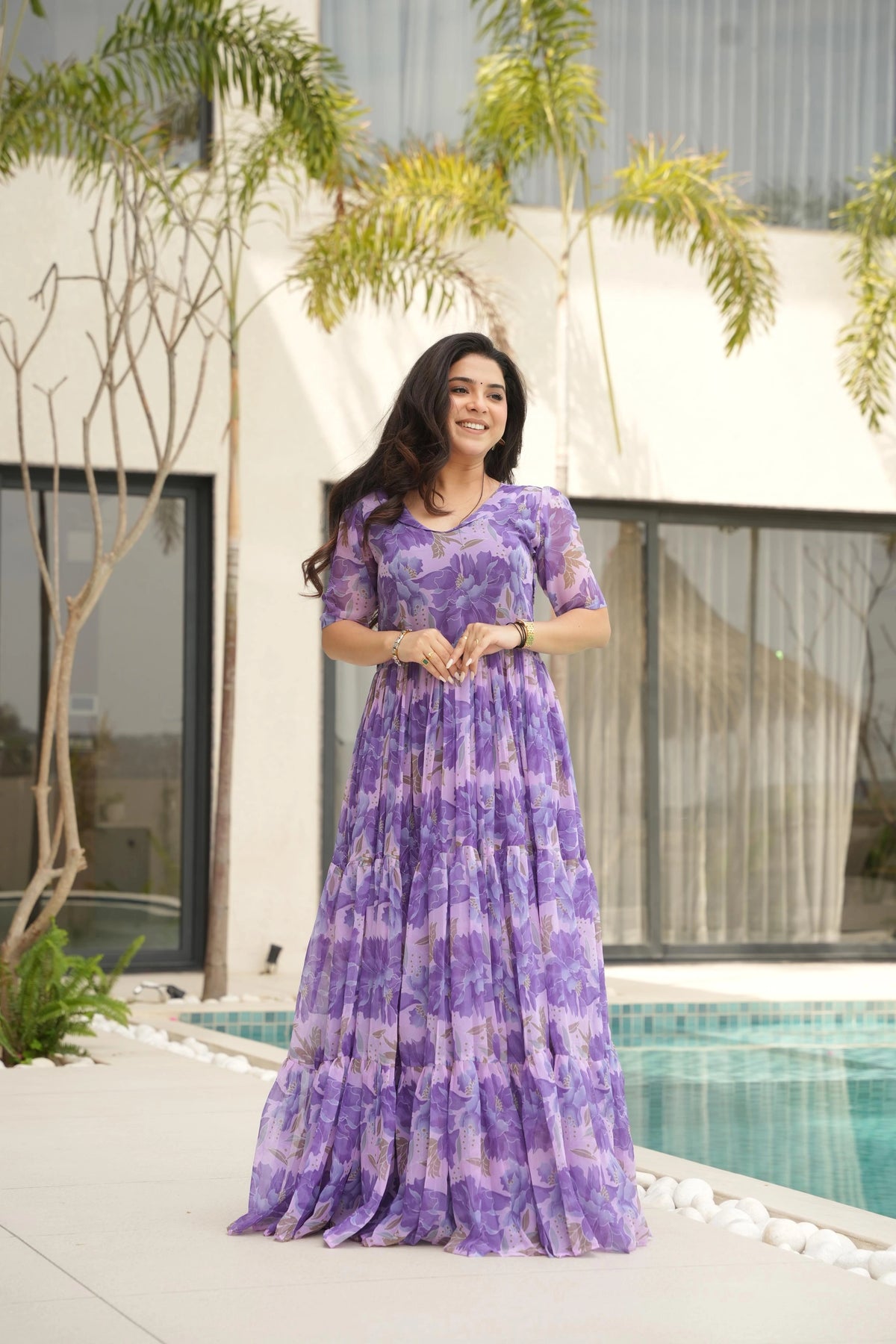 Woman in a purple dress standing by a pool with a building and trees in the background