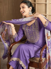 Woman in a purple embroidered outfit with a matching scarf, sitting on a wooden chair.