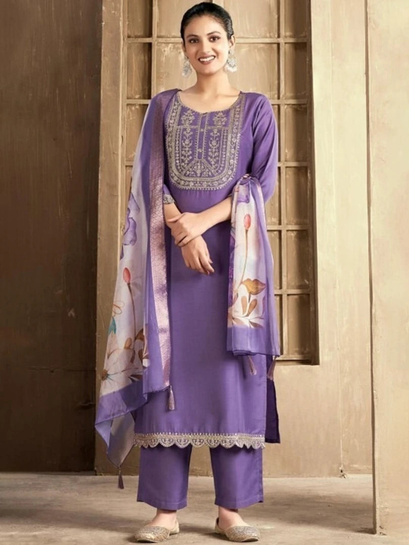 Woman wearing a purple traditional outfit with a matching dupatta, standing against a neutral wall.