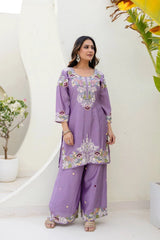Woman wearing a purple embroidered outfit standing against a white wall with decorative elements.