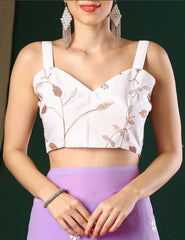 Woman wearing a white floral top with thin straps and a purple skirt against a dark background