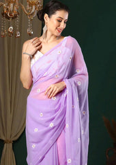 Woman wearing a light purple saree with white floral patterns against a dark background