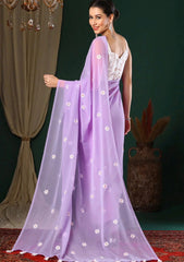 Woman wearing a lavender saree with white floral patterns against a dark green curtain.
