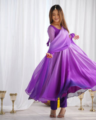 A woman twirls in a long purple ombre Anarkali suit, causing the fabric to flare out, while she looks down with a smile.