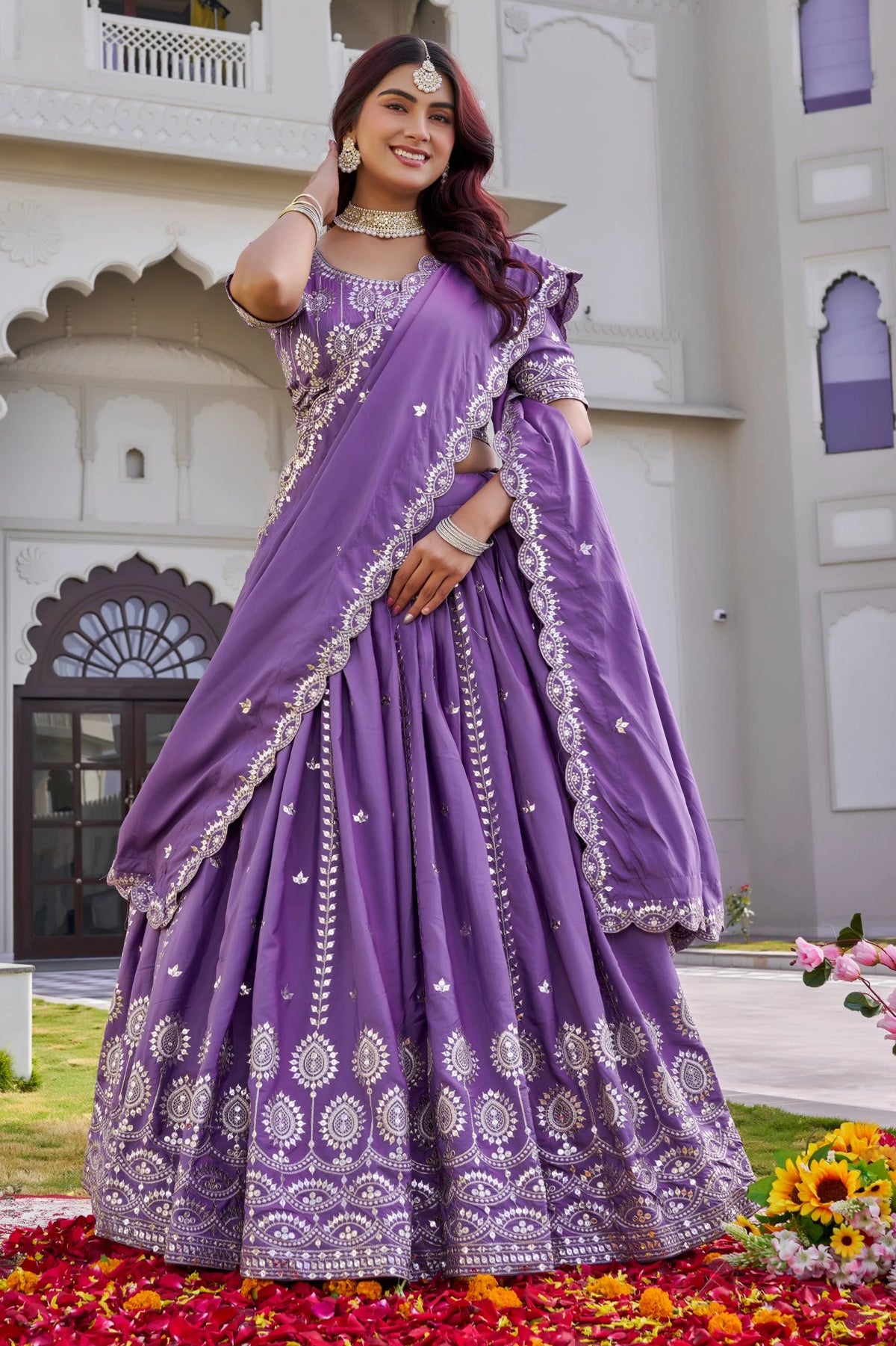 Woman in a purple saree with white patterns standing outdoors.