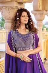 Woman in a purple traditional outfit with intricate designs standing in front of decorative columns.