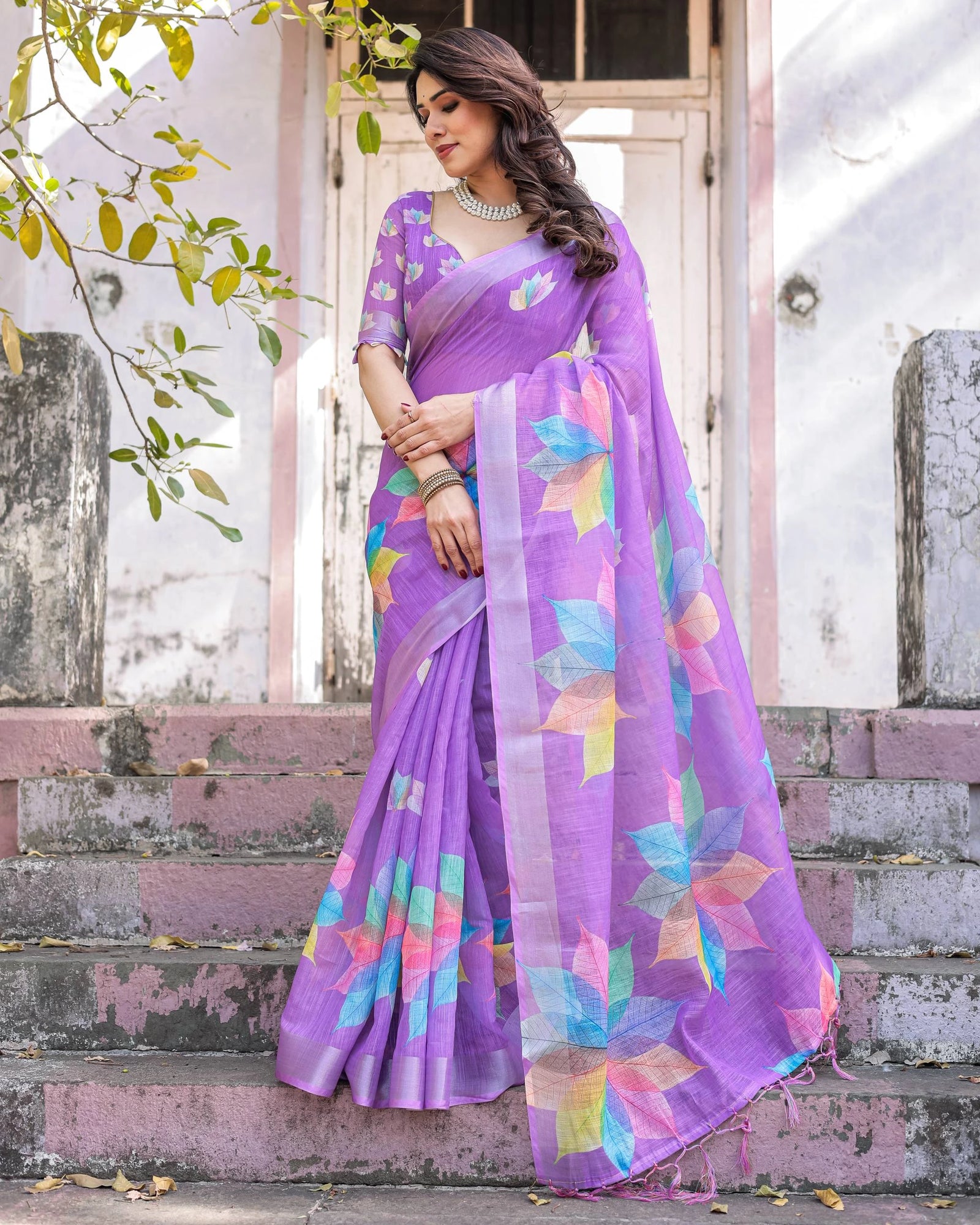 Woman wearing a purple saree with a colorful pattern, standing outdoors.