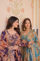 Two women in traditional embroidered dresses standing against a decorative wall.