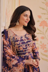 Woman wearing a floral and embroidered traditional outfit with jewelry against a floral wall.