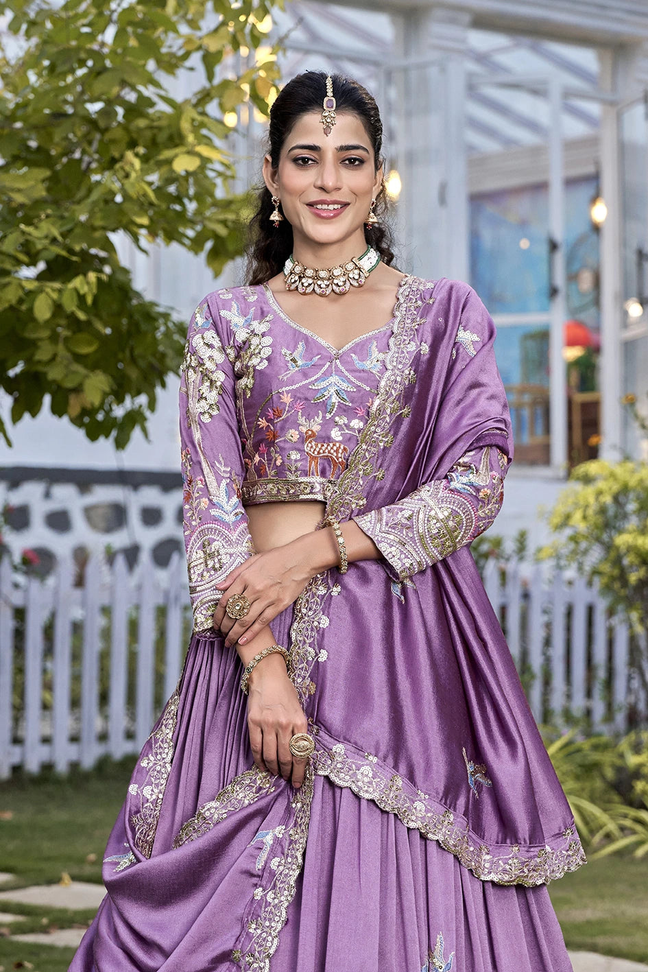Woman in a purple traditional outfit with floral patterns standing outdoors.