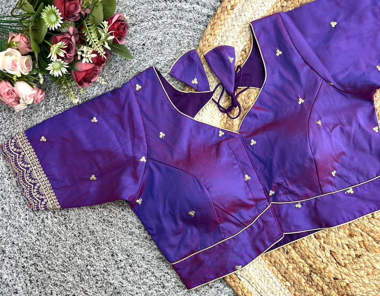 Purple blouse with gold embroidery on a textured surface with flowers in the background