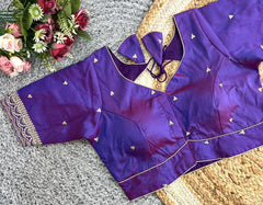 Purple blouse with gold embroidery on a textured surface with flowers in the background