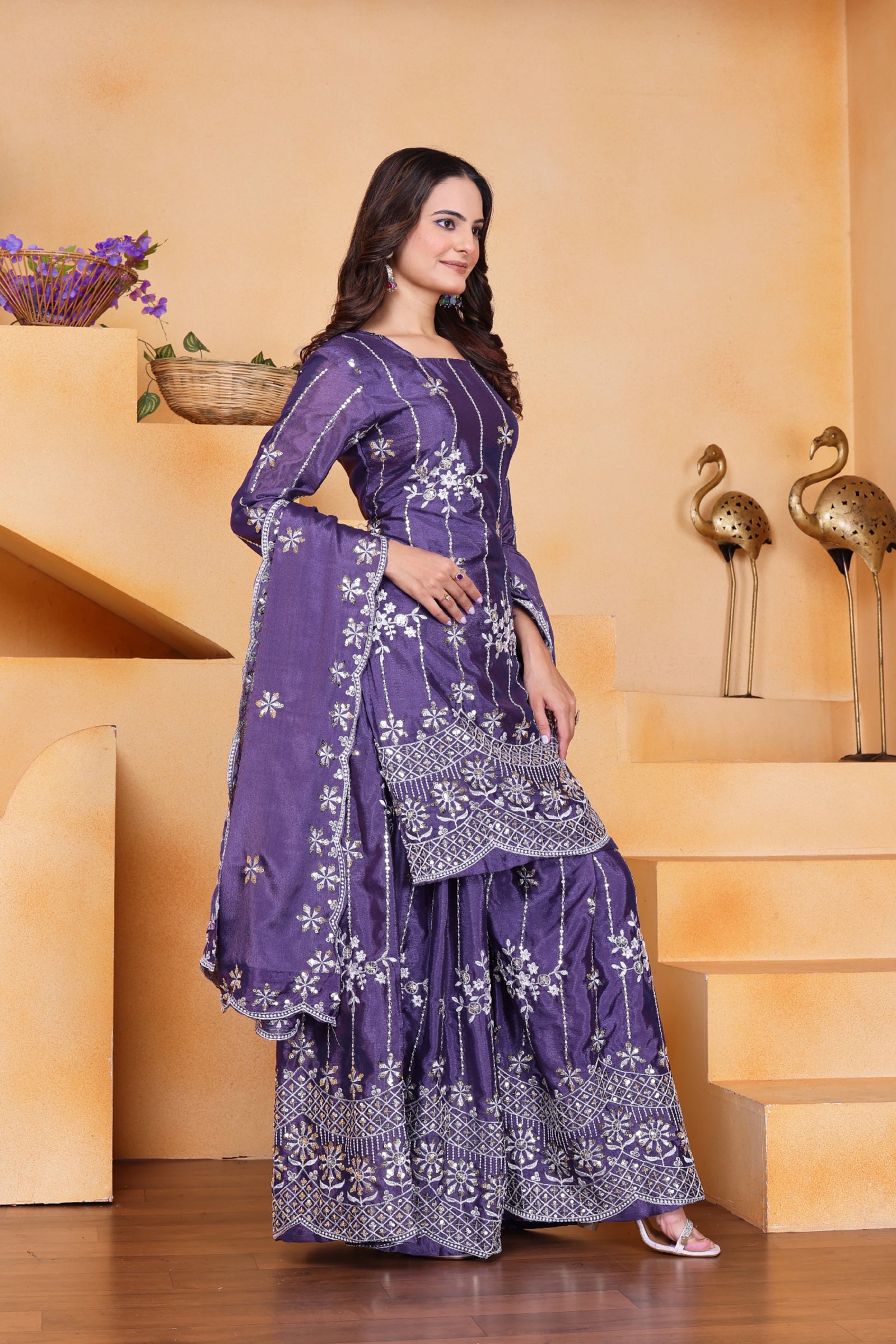 Woman in a purple traditional outfit standing in a decorative indoor setting.