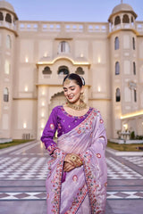 Woman in a purple saree standing in front of an architectural building.