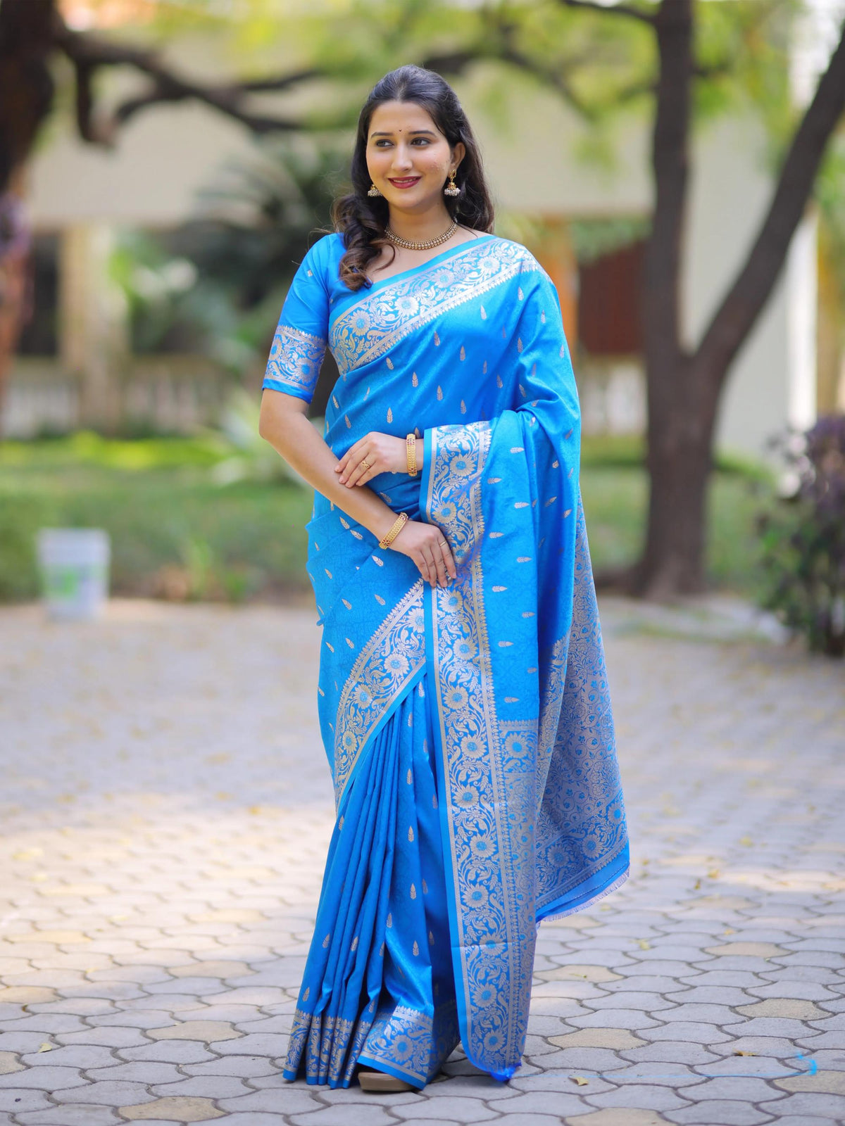 Woman wearing a blue saree with a white border outdoors.