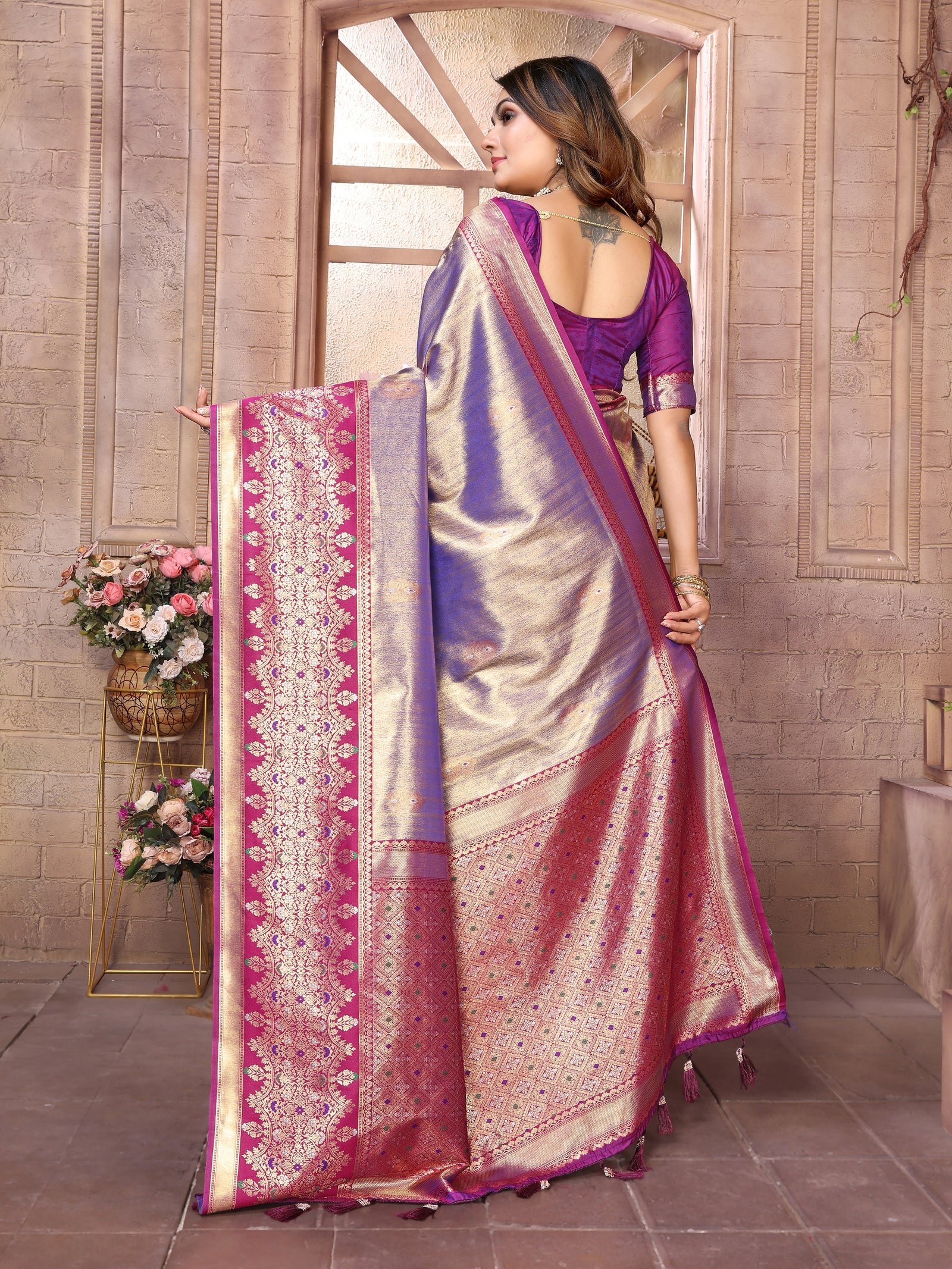 Woman holding a traditional saree with intricate patterns in a decorative setting.