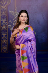 Woman wearing a traditional purple saree with colorful patterns against a decorative blue background