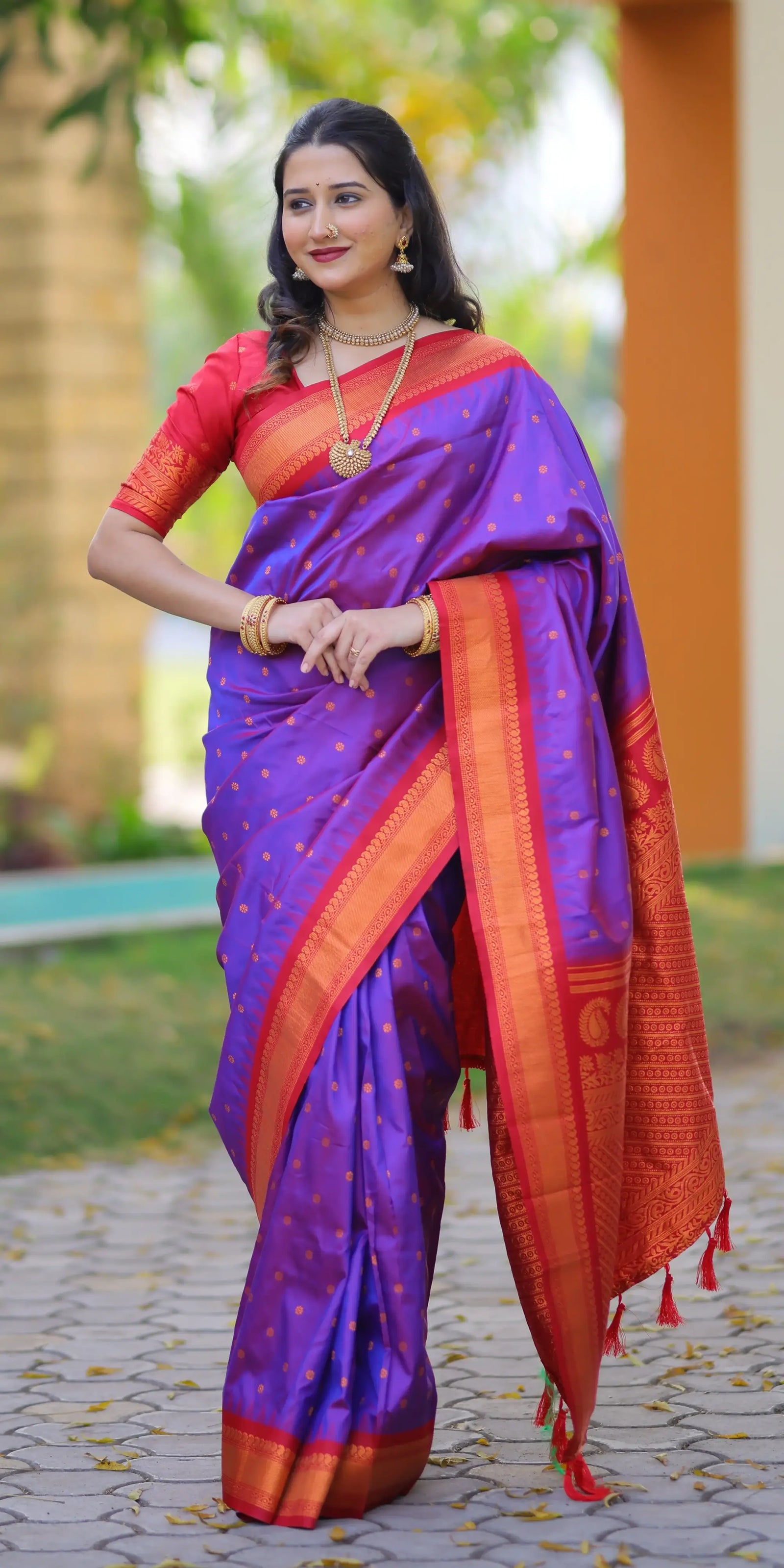 Woman wearing a purple and orange saree with a blurred outdoor background