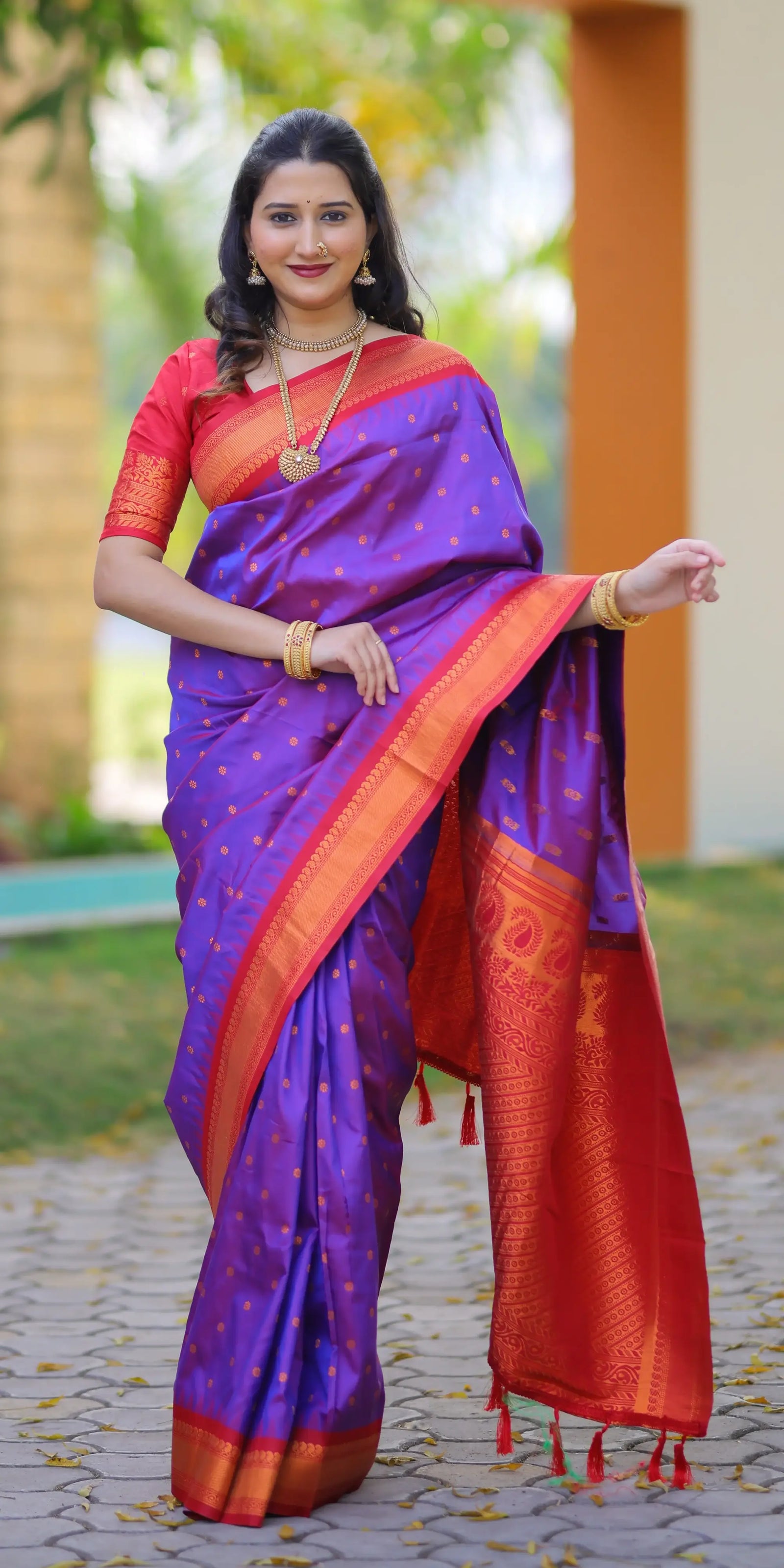 Woman wearing a purple and orange saree with a blurred outdoor background