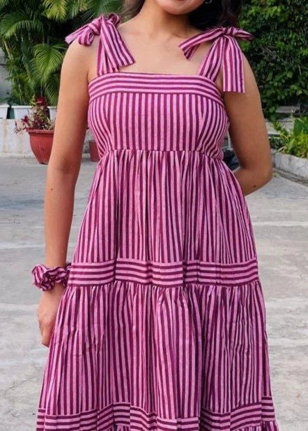Person wearing a pink and white striped dress with bow straps outdoors.
