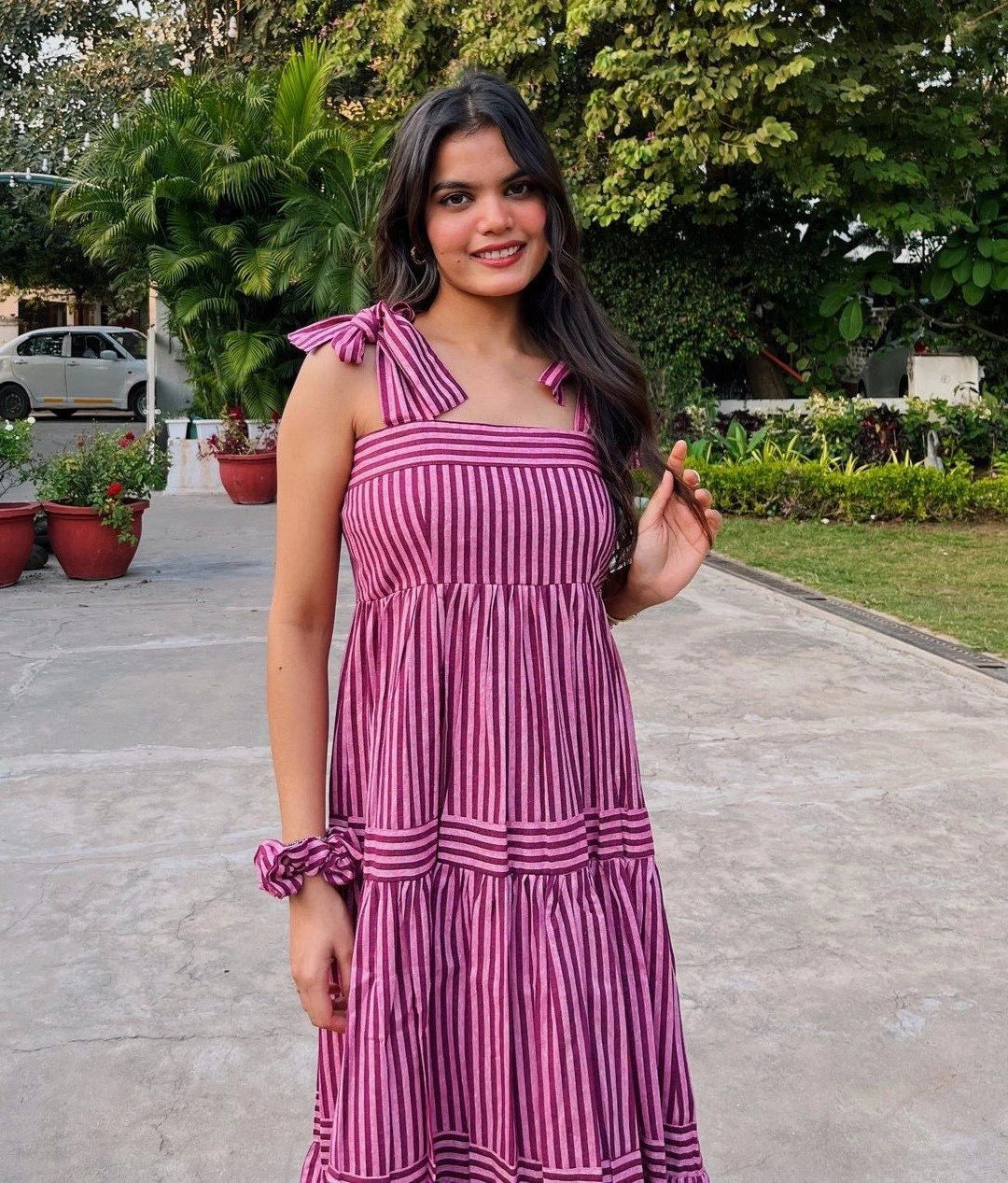Woman in a pink and white striped dress standing outdoors with greenery in the background
