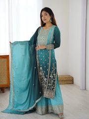 Woman wearing a traditional outfit with a turquoise dupatta and embroidered dress indoors.