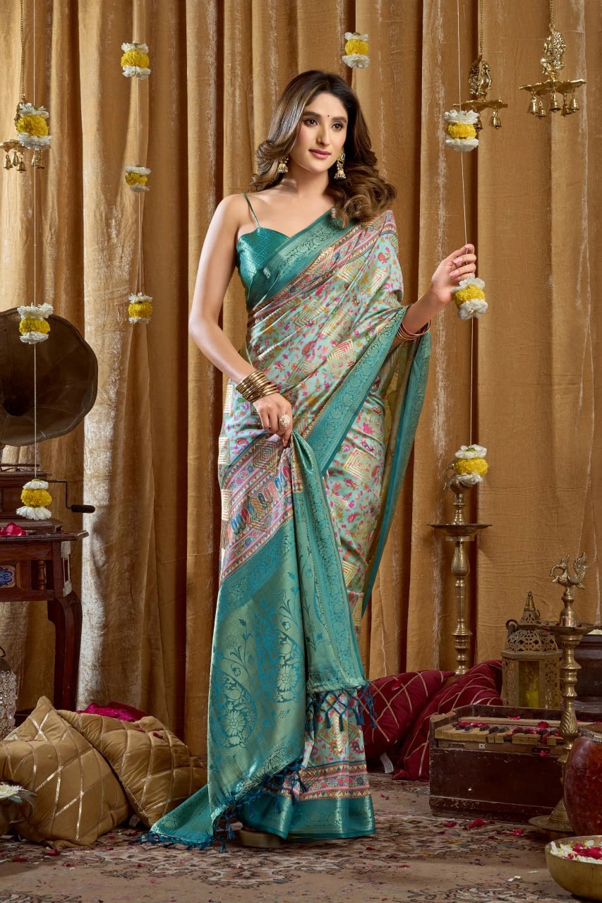 Woman in a teal saree with a patterned blouse standing in a decorated room.
