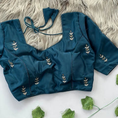 Blue embroidered top on a textured surface with green leaves.