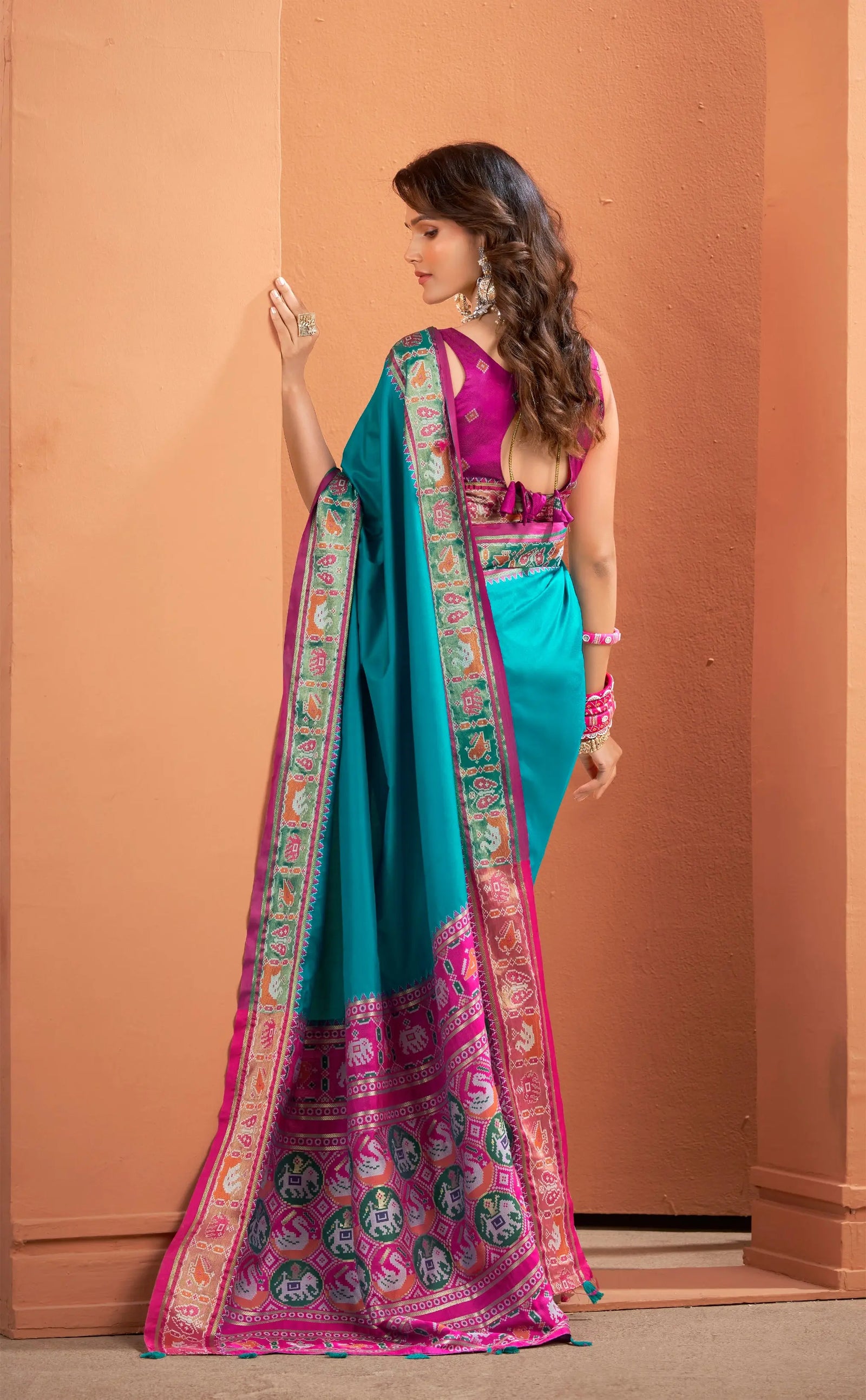 Woman wearing a vibrant turquoise and pink saree with a plain background