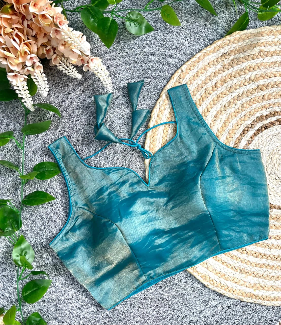 Teal bikini set on a textured surface with leaves and flowers around